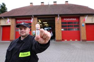 strażak OSP w mundurze z fiolką szczepionki w dłoni