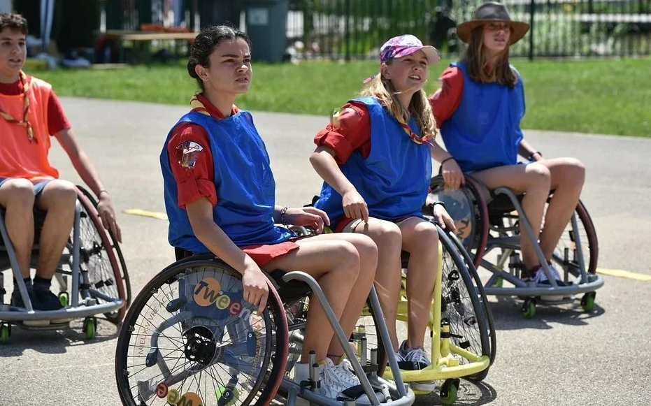 na zdjęciu trzy dziewczynki w sportowych letnich strojach, wszystkie siedzą na wózkach inwalidzkich